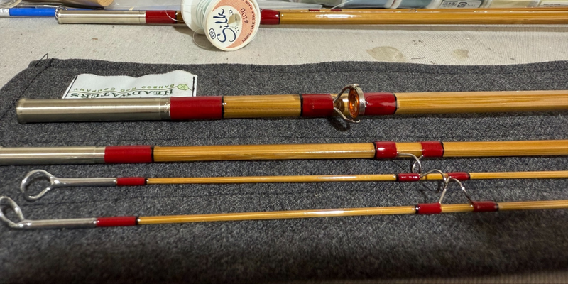 sections of a hand-built Headwaters bamboo fly rod on the bench — red thread wraps, an agate stripping guide, nickel-silver ferrules and a spool of silk
